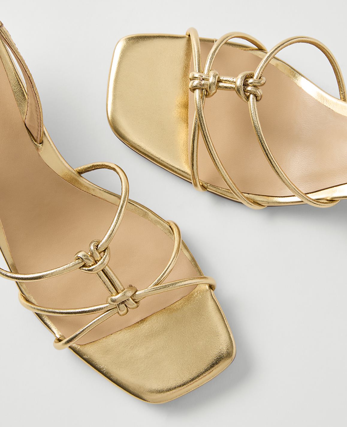 A pair of golden strappy sandals with knotted details are displayed against a plain white background.
