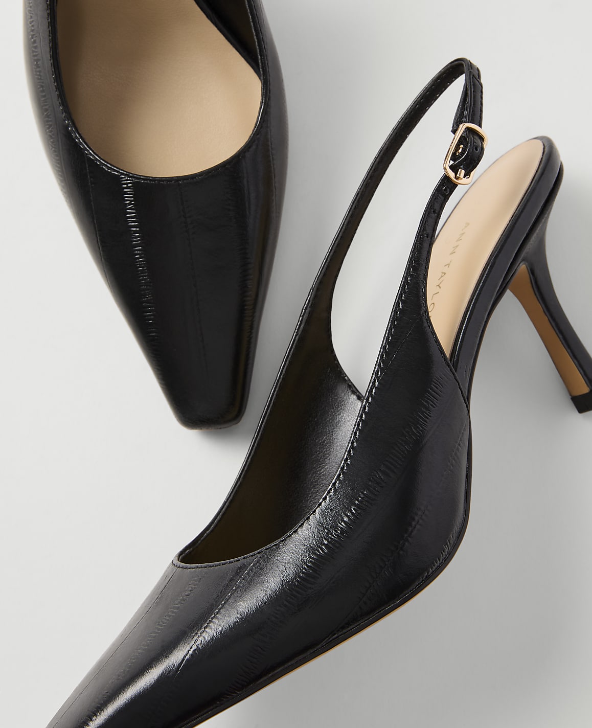 A pair of glossy black slingback heels with pointed toes are displayed against a plain white background.
