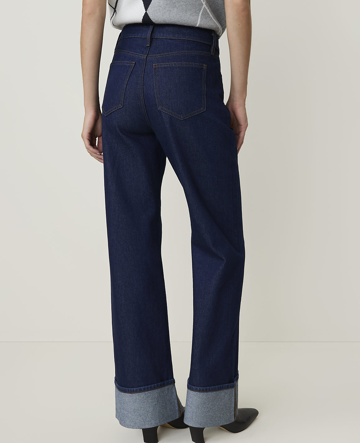 Dark wash denim jeans with wide, cuffed hems are worn against a plain, light background.