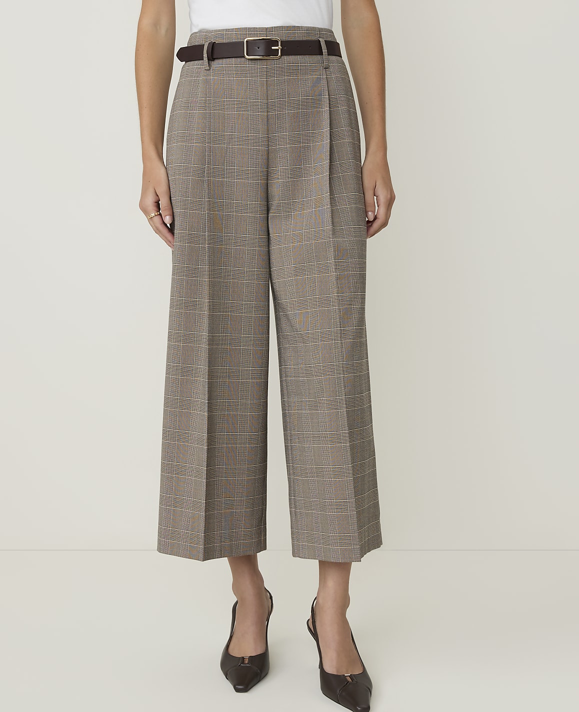 A person stands in the foreground wearing plaid culottes and heels against a plain white background.