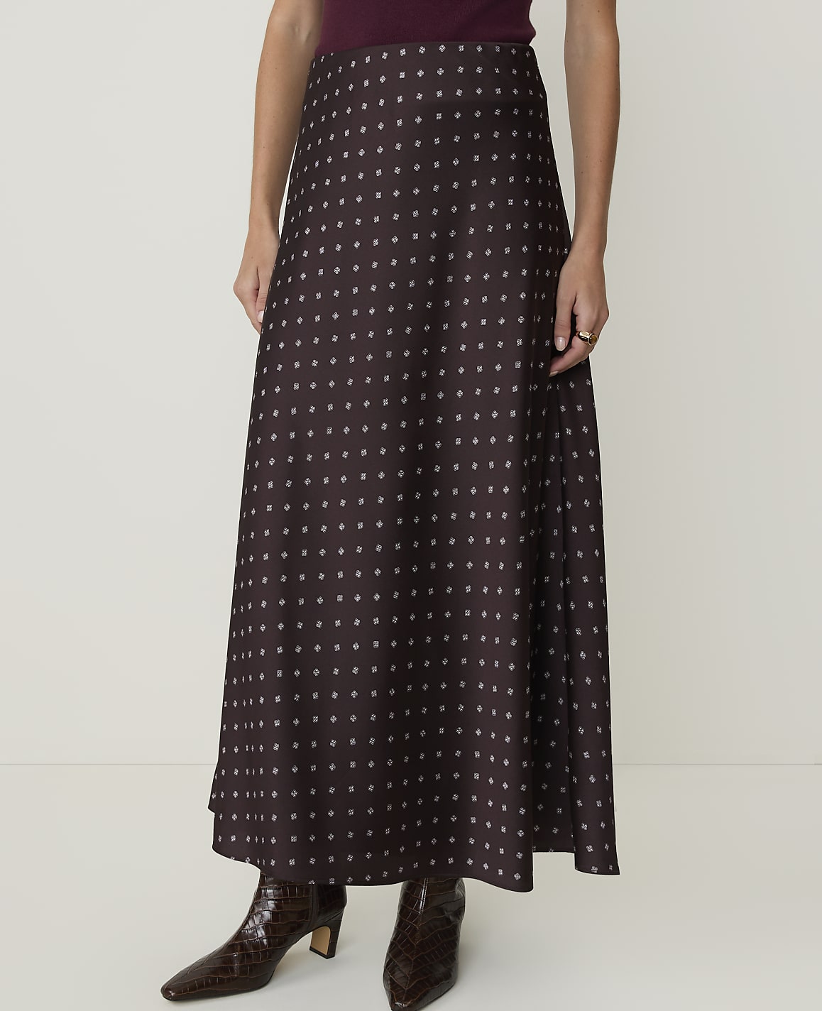 A woman in a patterned maxi skirt and croc-embossed boots stands against a plain white background.