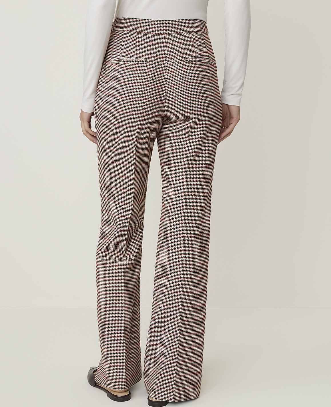 A person wearing plaid flared pants stands against a plain white background.