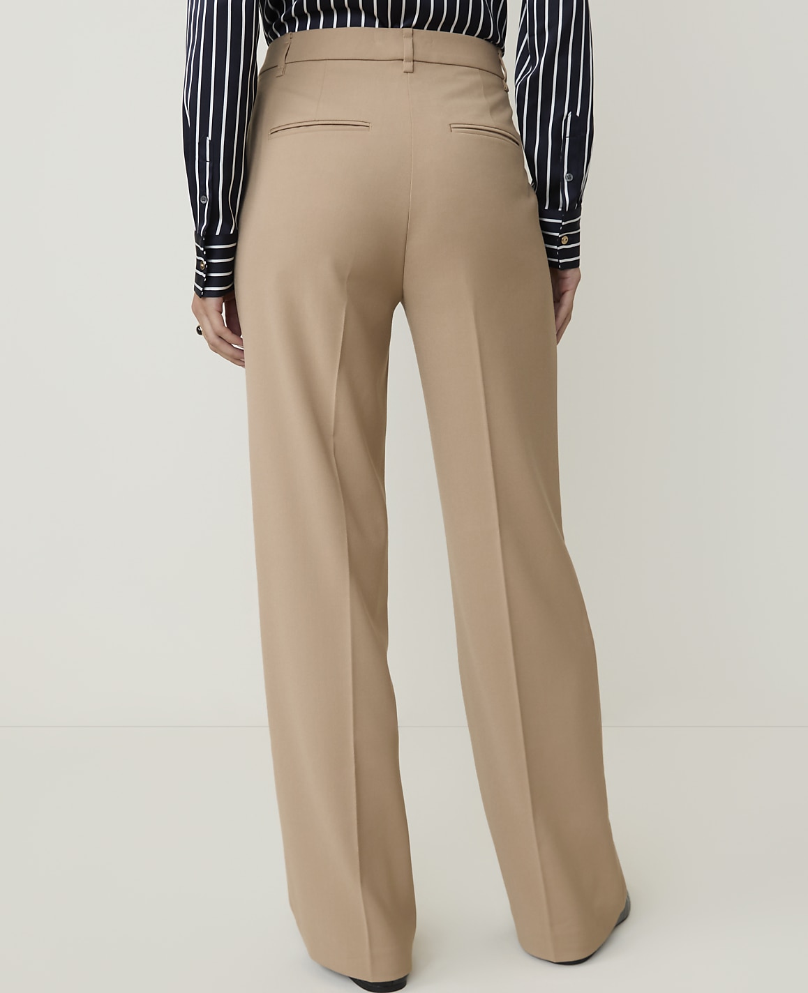 A person wearing tan wide-leg trousers and a striped shirt stands against a plain, light background.
