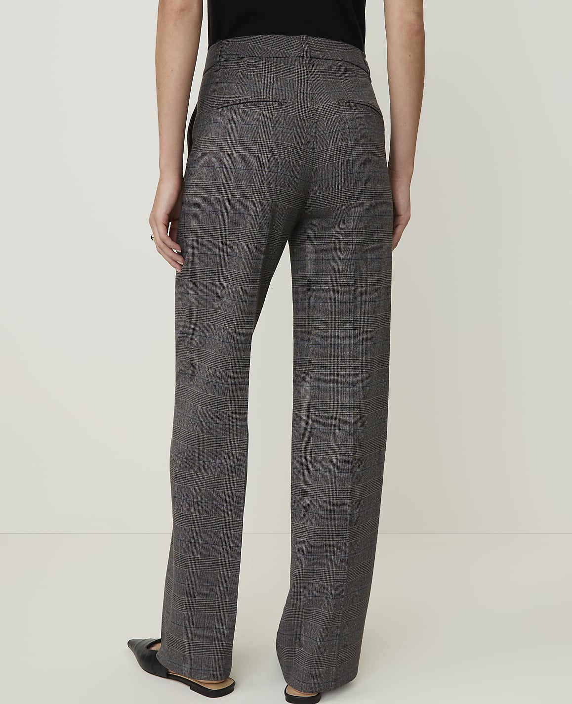 A person wearing plaid trousers stands against a plain white background.