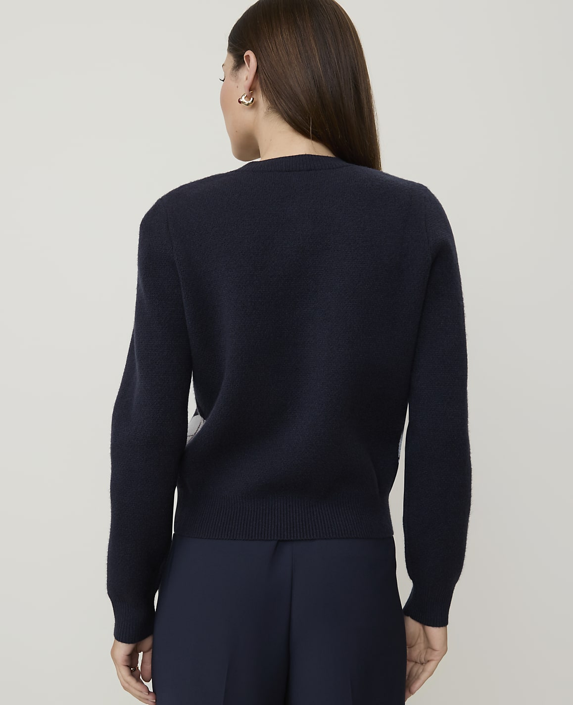 A woman in a dark blue sweater and pants stands against a plain, light gray background.