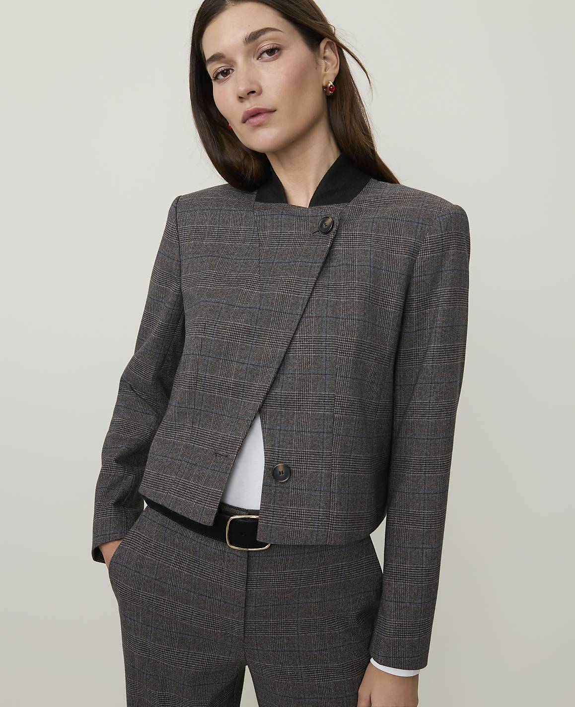 A woman in a plaid jacket and pants stands against a plain, light gray background.