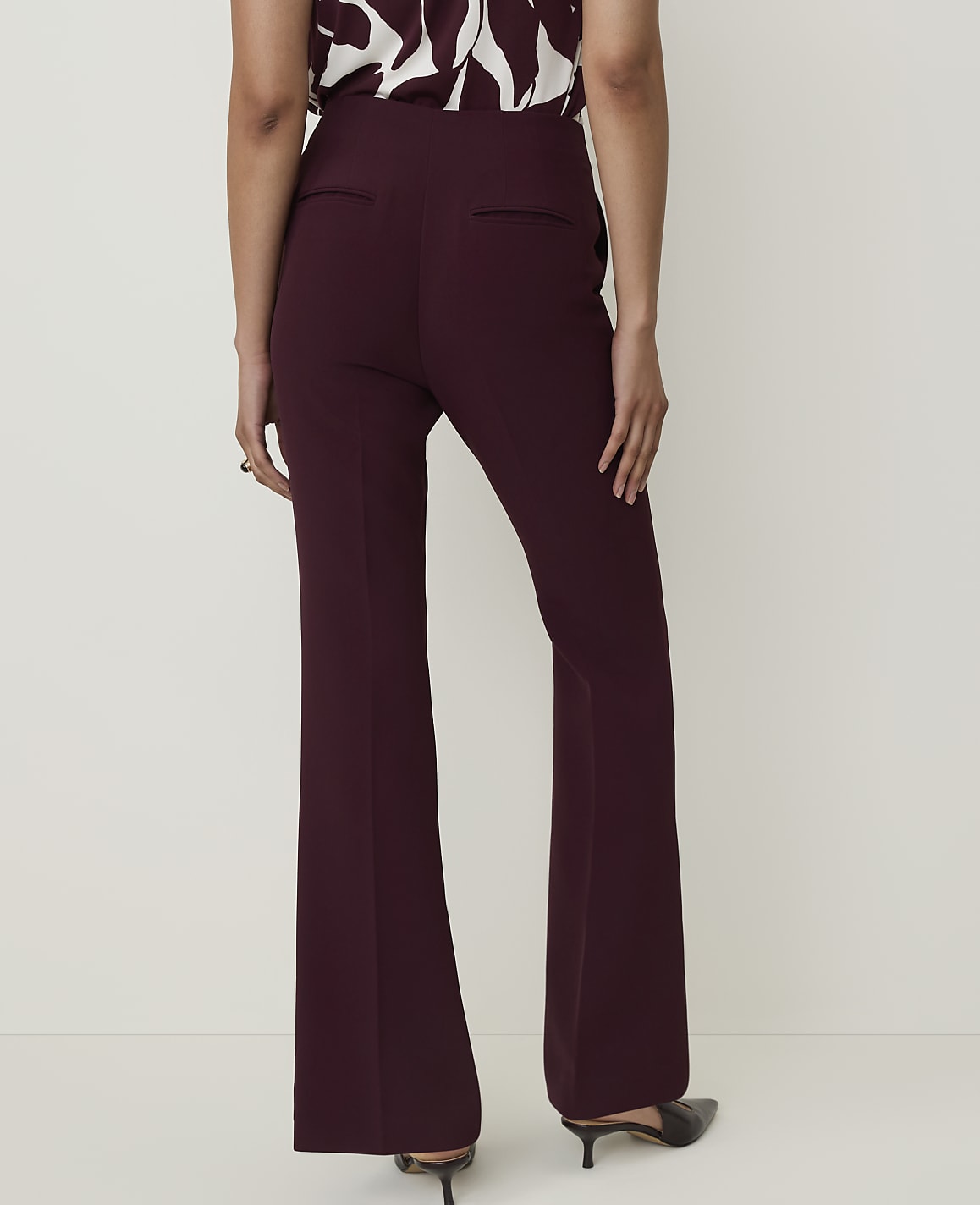 A person wearing burgundy flared trousers and a patterned top stands against a plain white background.