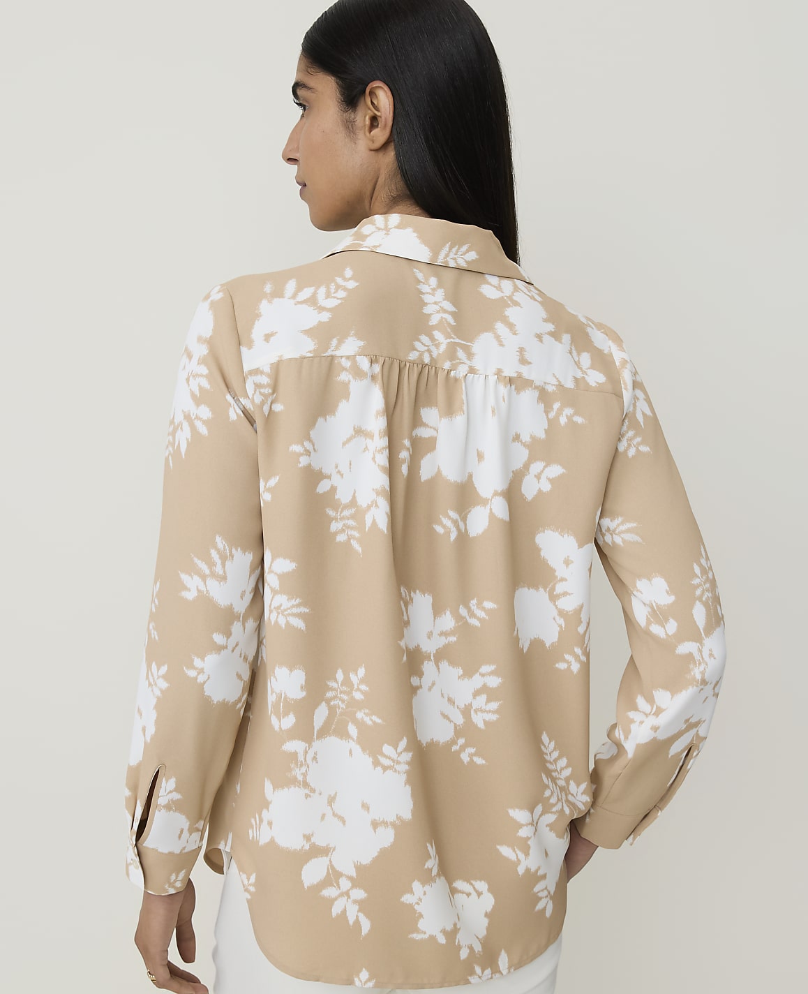 A woman in a tan floral blouse stands against a plain white background.