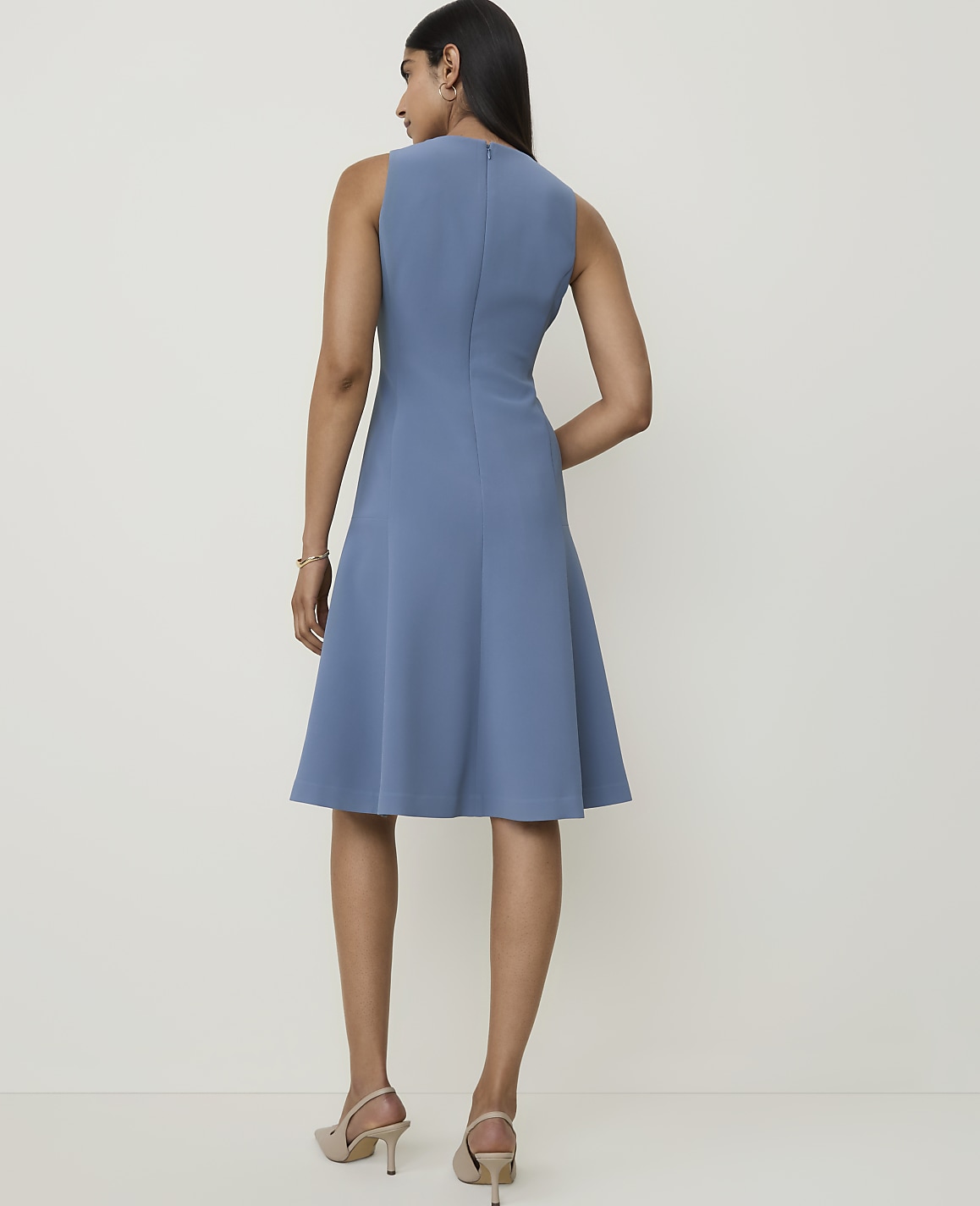 A woman in a blue sleeveless dress stands against a plain, light-colored background.