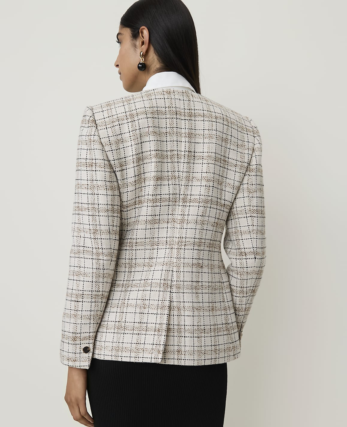 A woman in a tweed blazer stands against a plain, light-colored background.