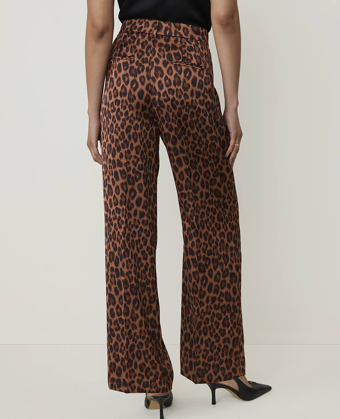 A person wearing leopard print wide-leg pants and black heels stands against a plain, light-colored background.