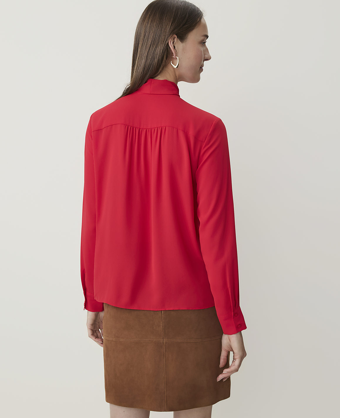 A woman in a red blouse and brown skirt stands against a plain white background.