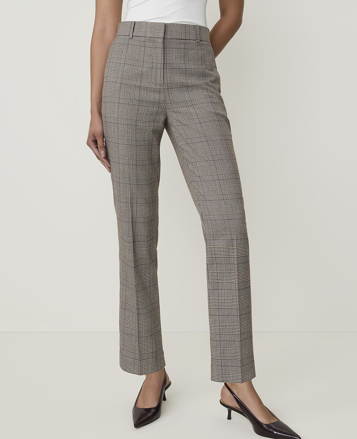 A person stands in the foreground wearing plaid trousers and black heels against a plain, light-colored background.