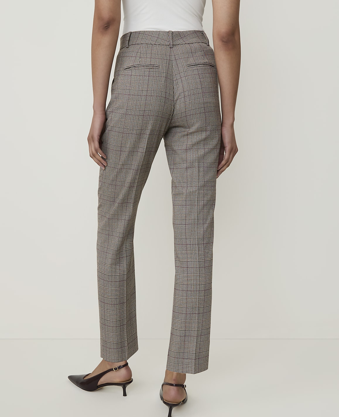 A person wearing plaid trousers and slingback heels stands against a plain white background.