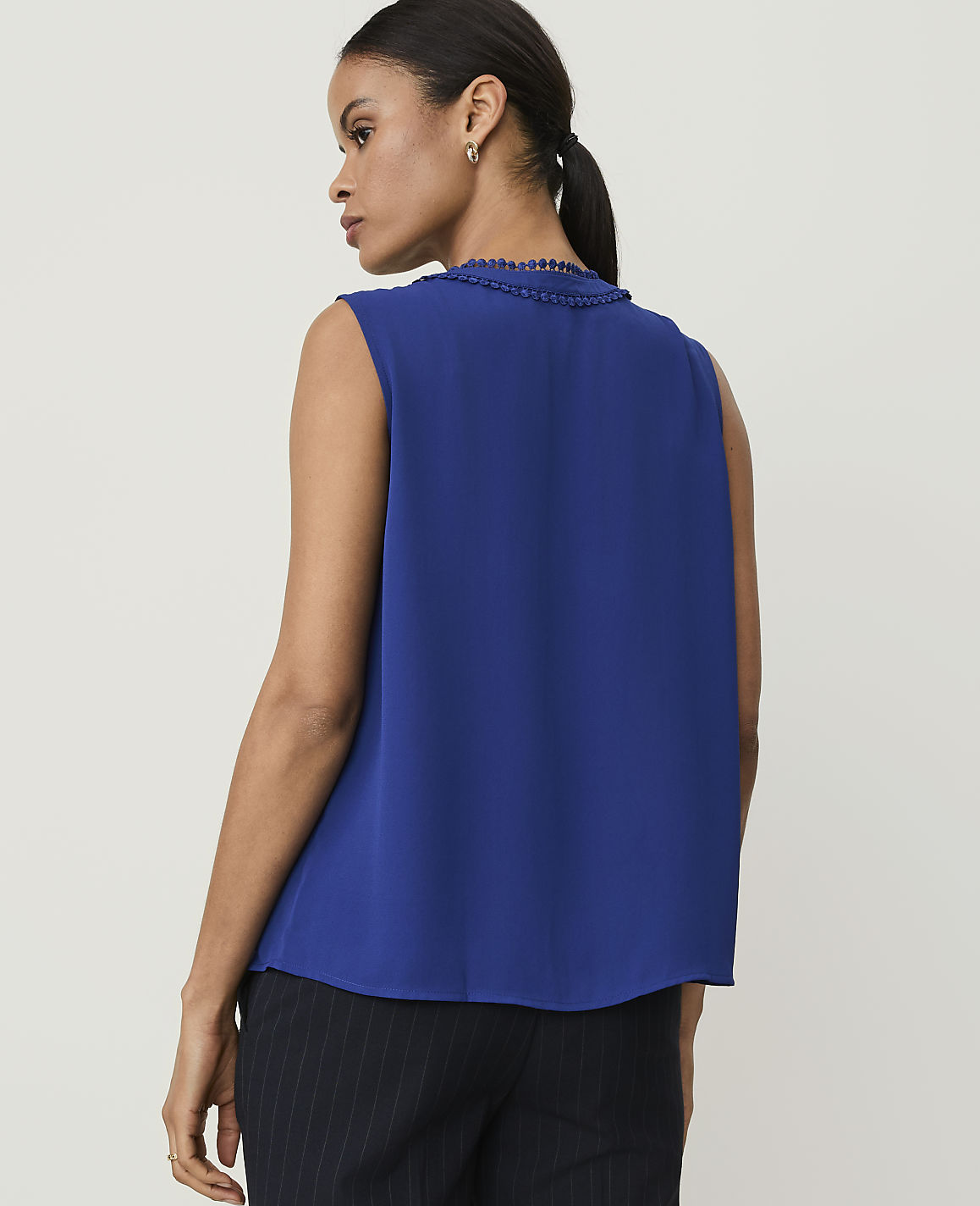 A woman in a blue sleeveless top and pinstripe pants stands against a plain white background.