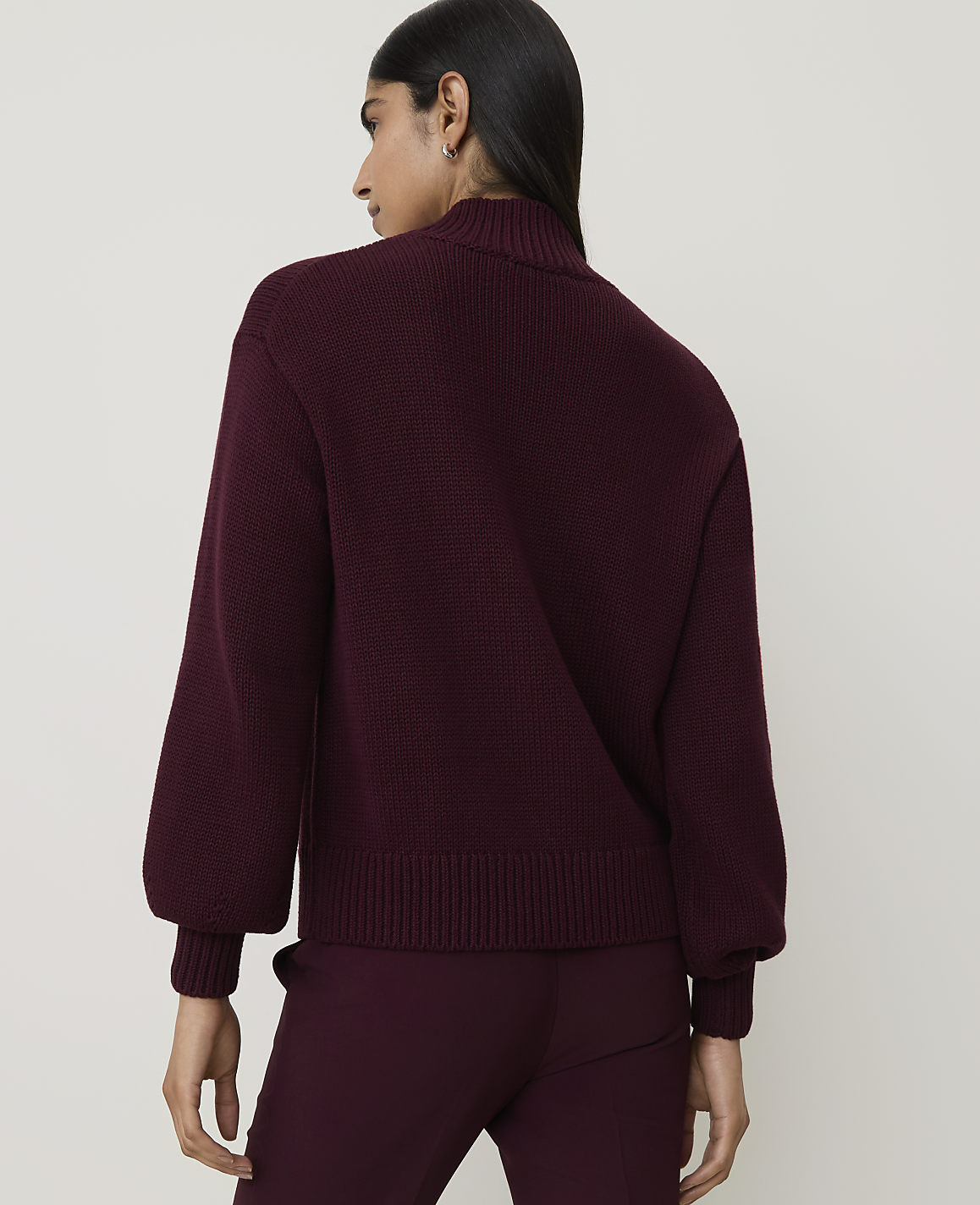 A woman in a burgundy sweater and pants stands against a plain white background.
