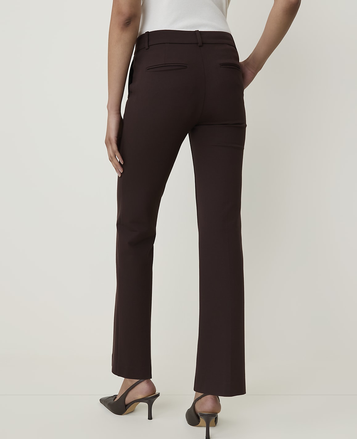 A person wearing brown dress pants and heels stands against a plain, light-colored background.