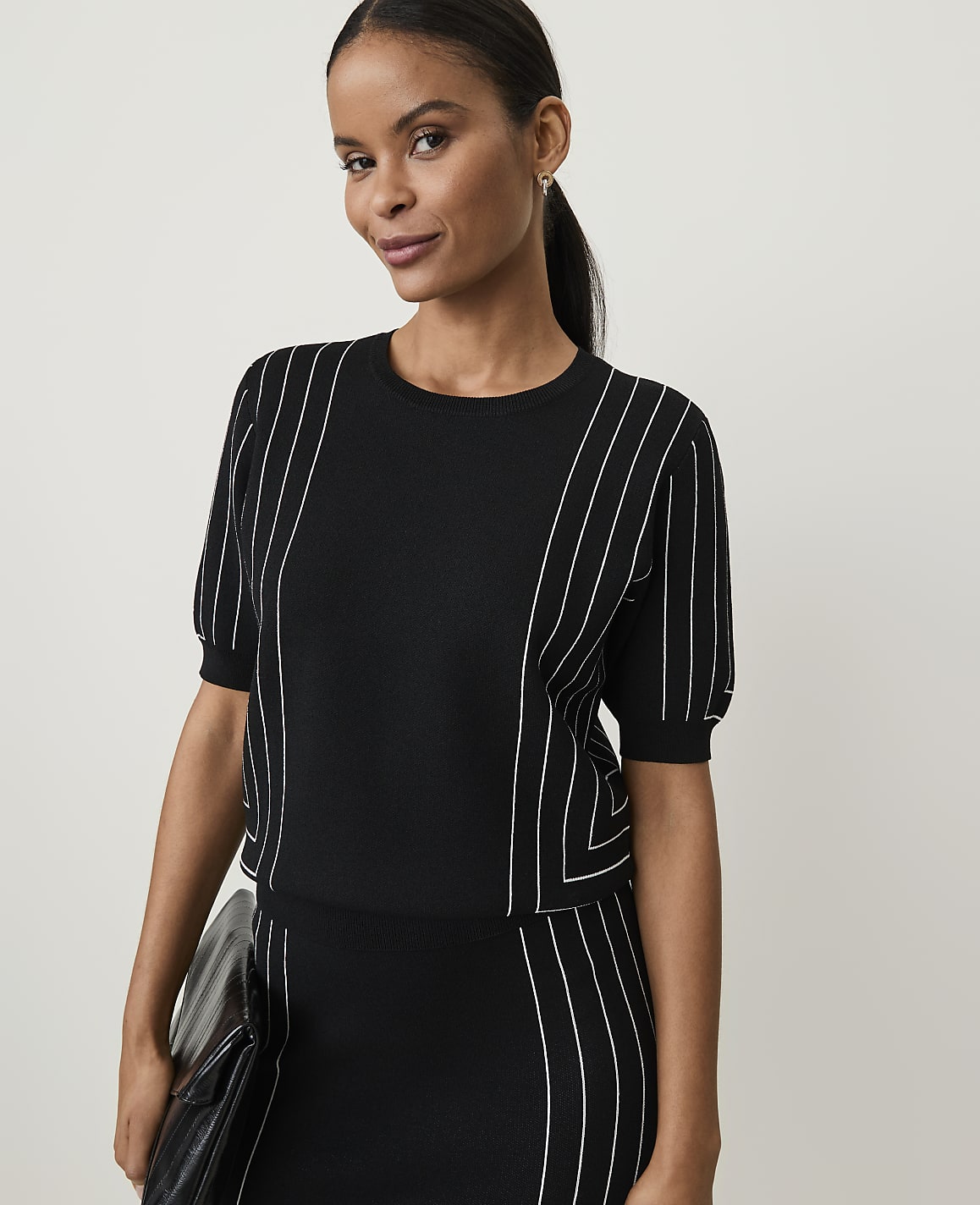 A woman in a black and white striped top and skirt stands against a plain white background.