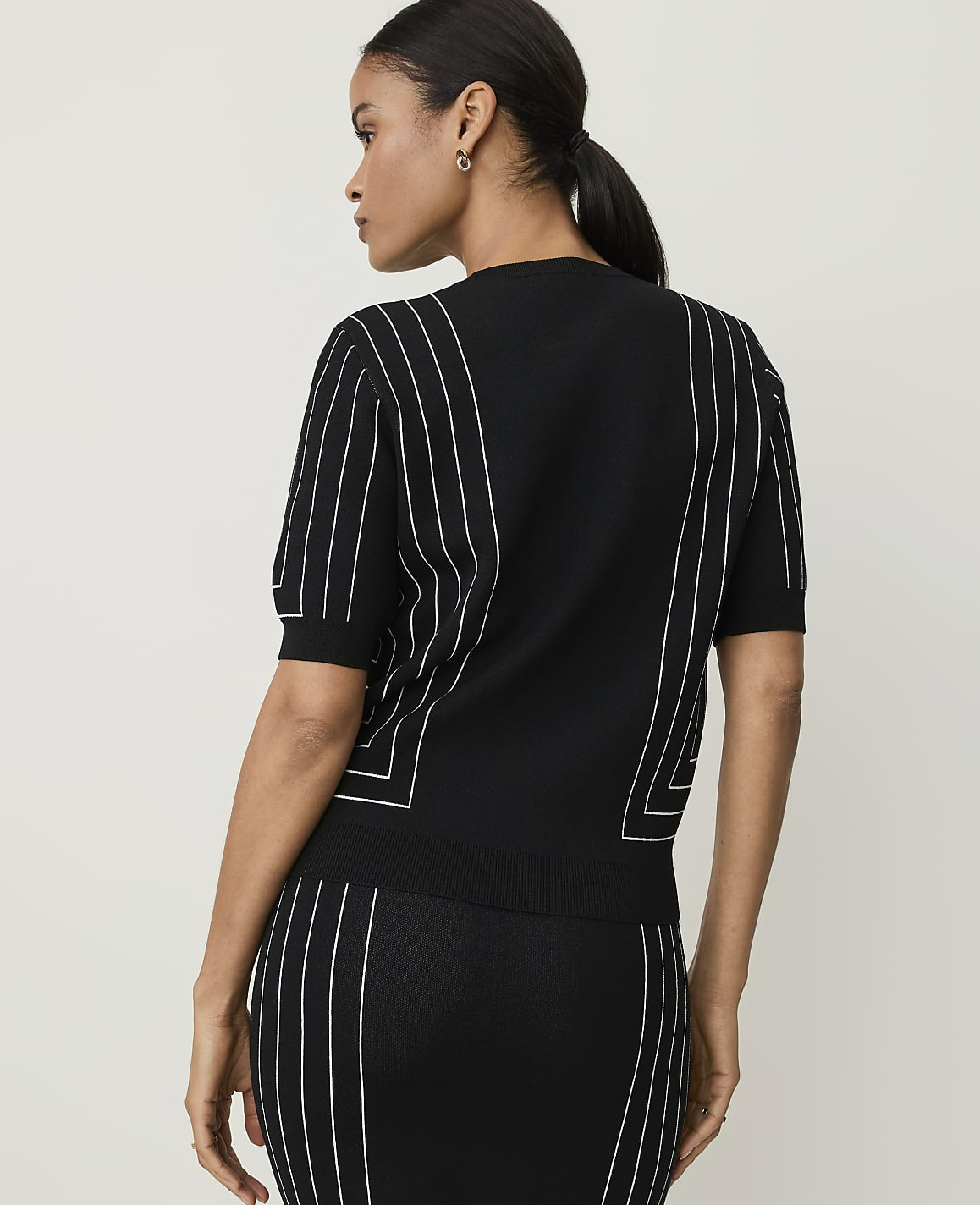 A woman in a black top with white pinstripes stands against a plain white background.