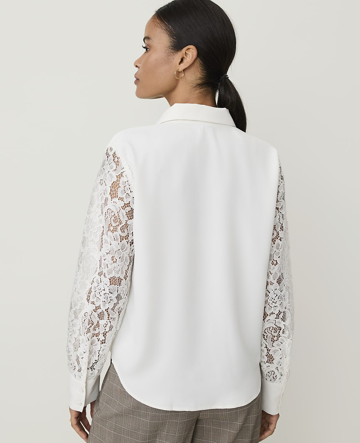A woman in a white blouse with lace sleeves stands against a plain white background.