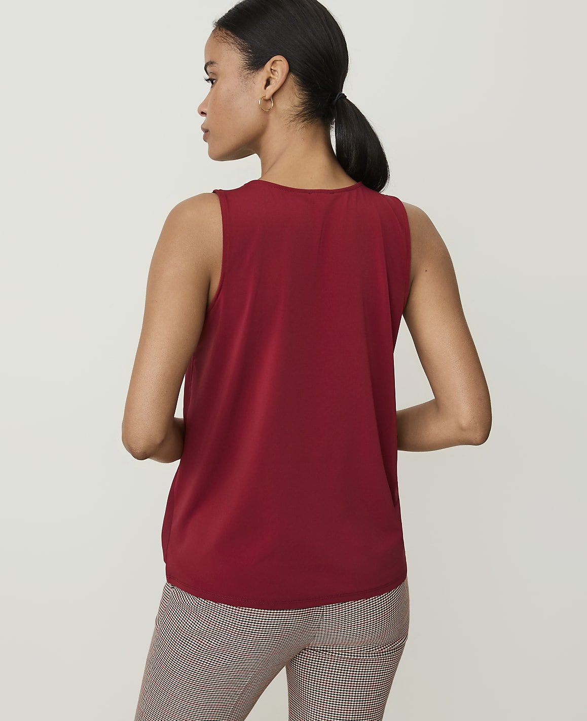 A woman in a red sleeveless top and patterned pants stands against a plain white background.