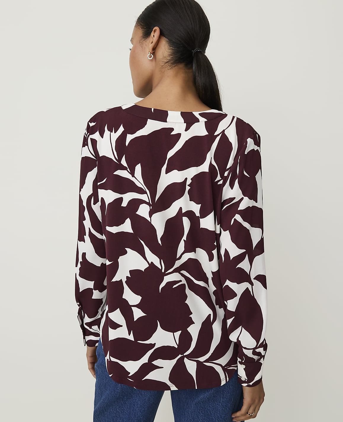 A woman in a maroon and white floral blouse stands against a plain white background.
