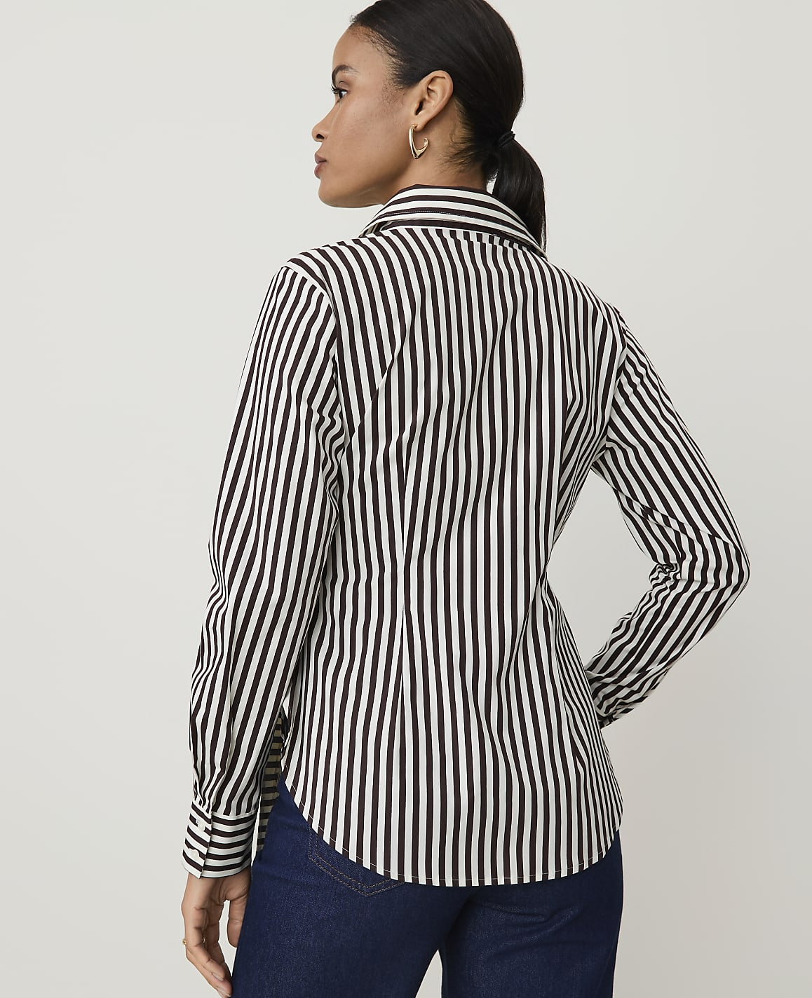 A woman in a black and white striped shirt stands against a plain white background.