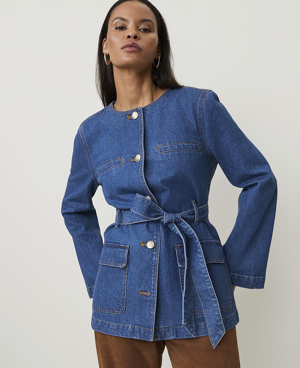A woman in a denim jacket stands against a plain white background.