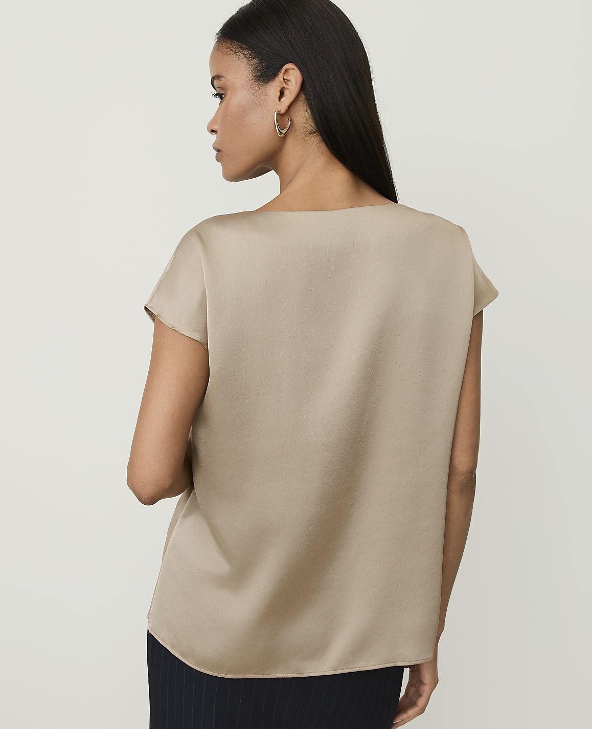 A woman in a tan satin top stands against a plain, light background.