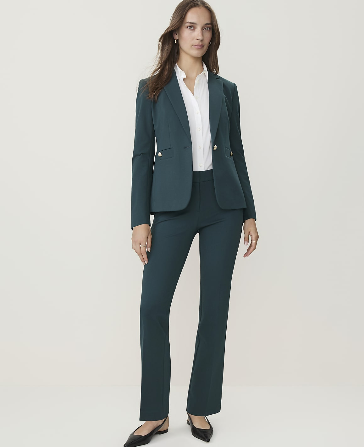 A woman in a teal pantsuit stands against a plain, light-colored background.