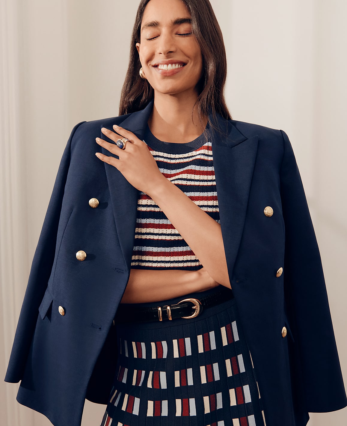 A smiling woman in a navy blazer and striped top poses against a plain, light-colored background.