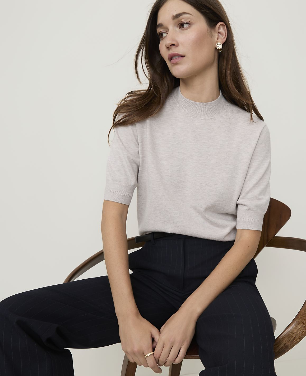 A blonde woman in a black turtleneck and denim jeans stands against a plain white background.