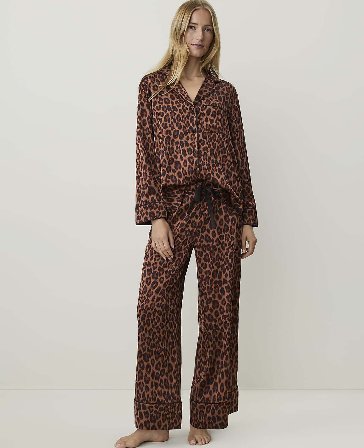 A woman in leopard print pajamas stands against a plain, light-colored background.