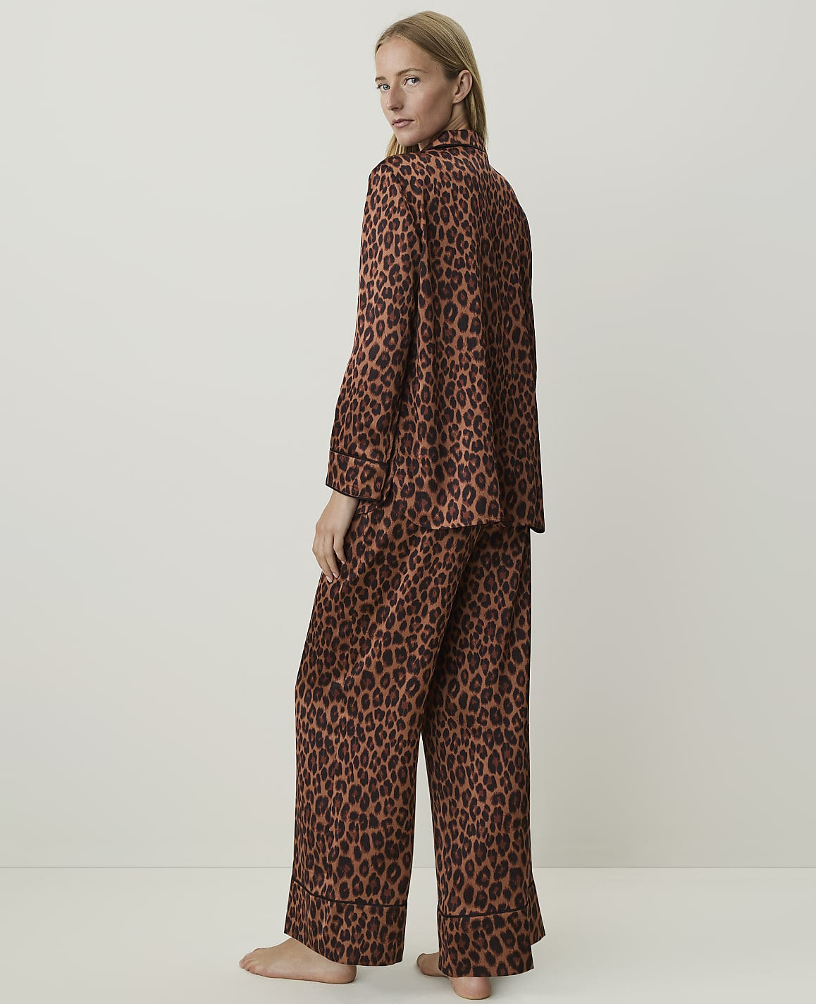 A woman in leopard print pajamas stands against a plain, light brown background.