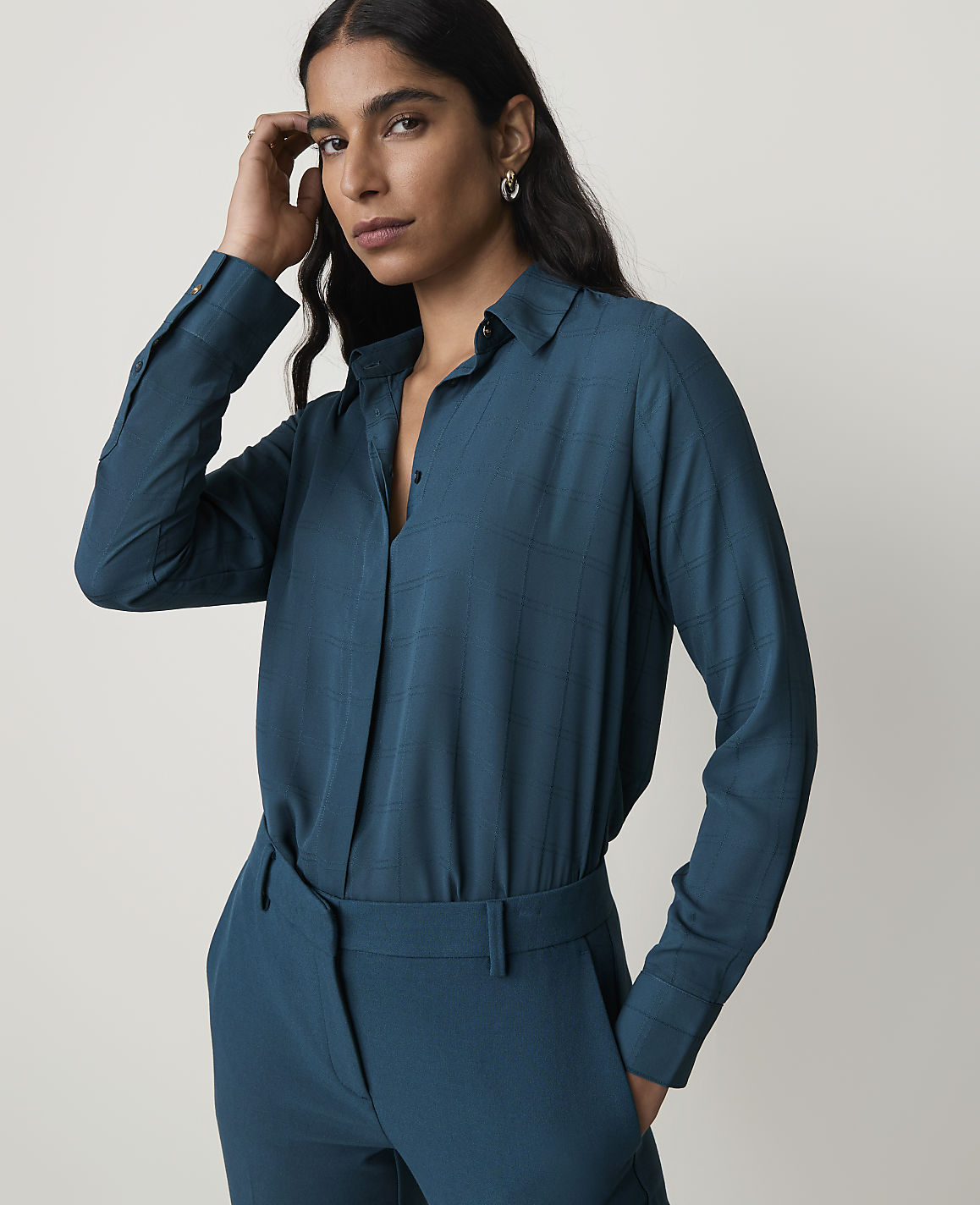 A woman in a teal blouse and matching pants stands against a plain gray background.