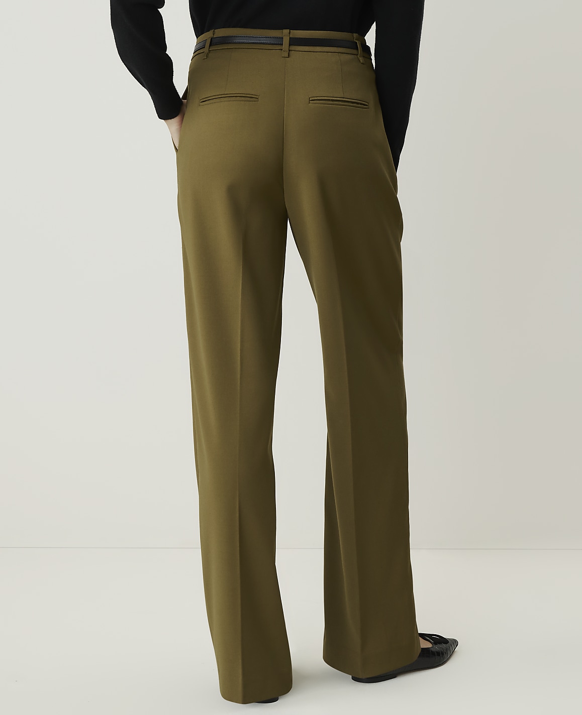 A person wearing olive green wide-leg trousers and black shoes stands against a plain white background.