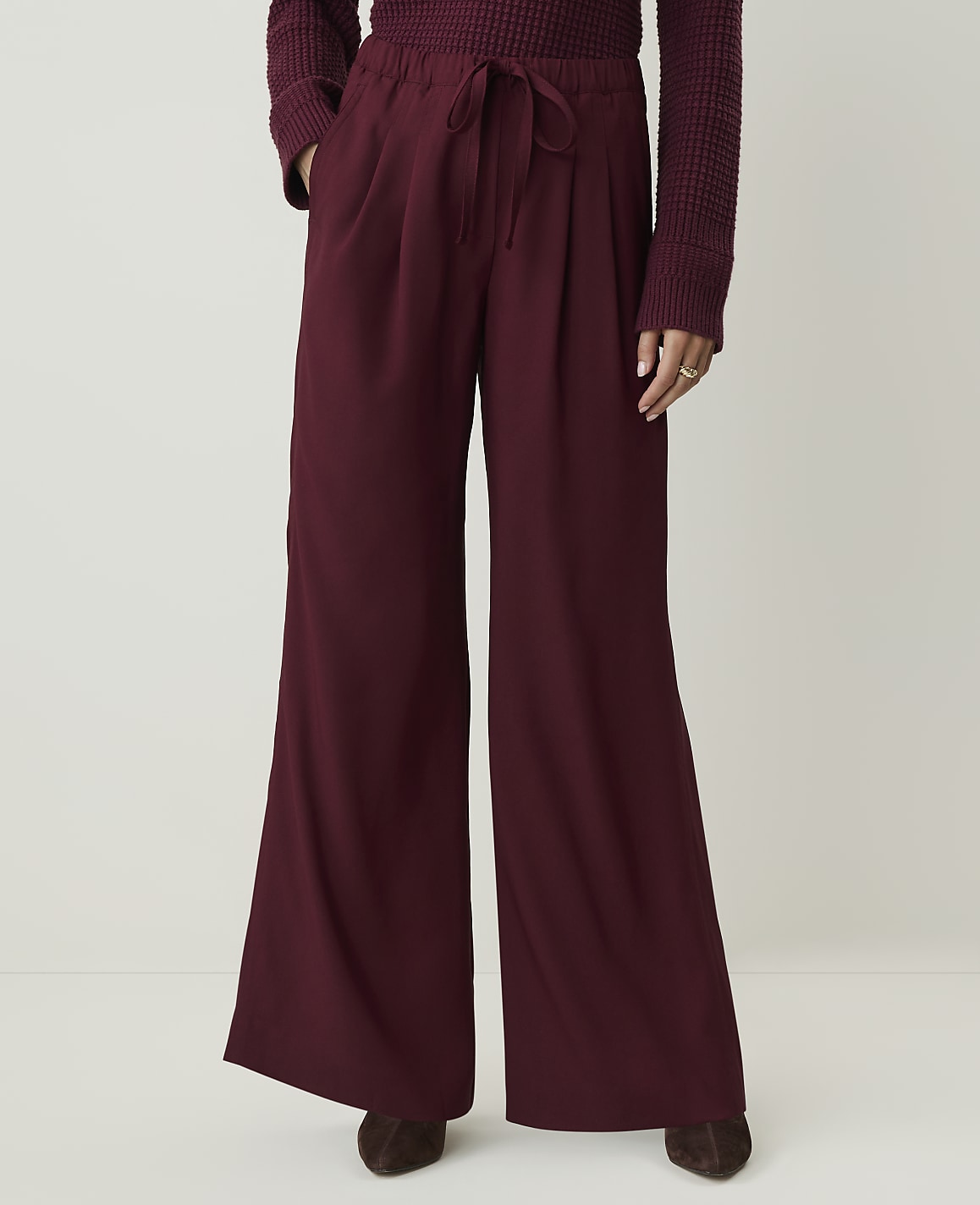A person stands in maroon wide-leg pants and a maroon sweater against a plain white background.