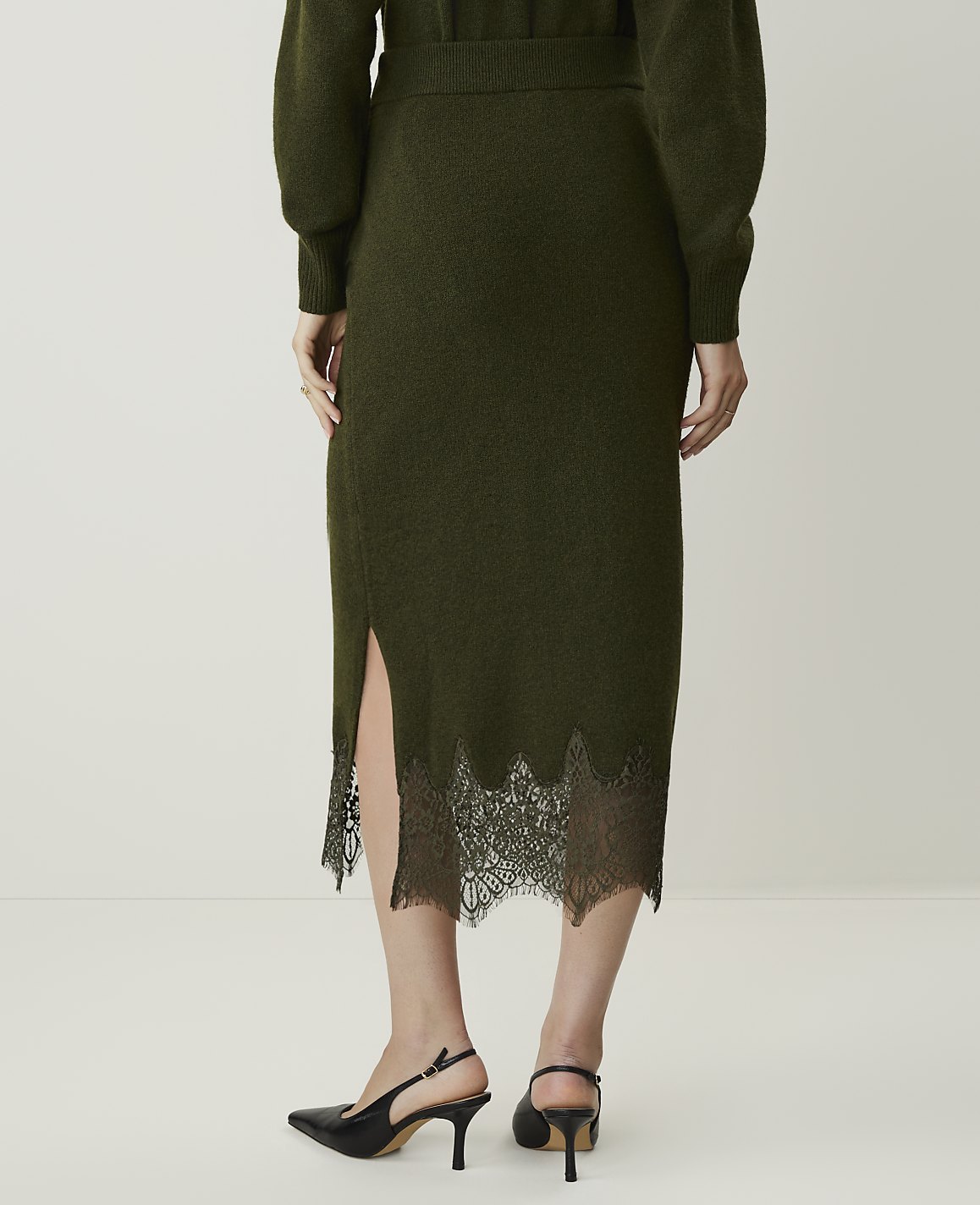 A person wearing a green knit skirt with a lace hem and black slingback heels stands against a plain white background.