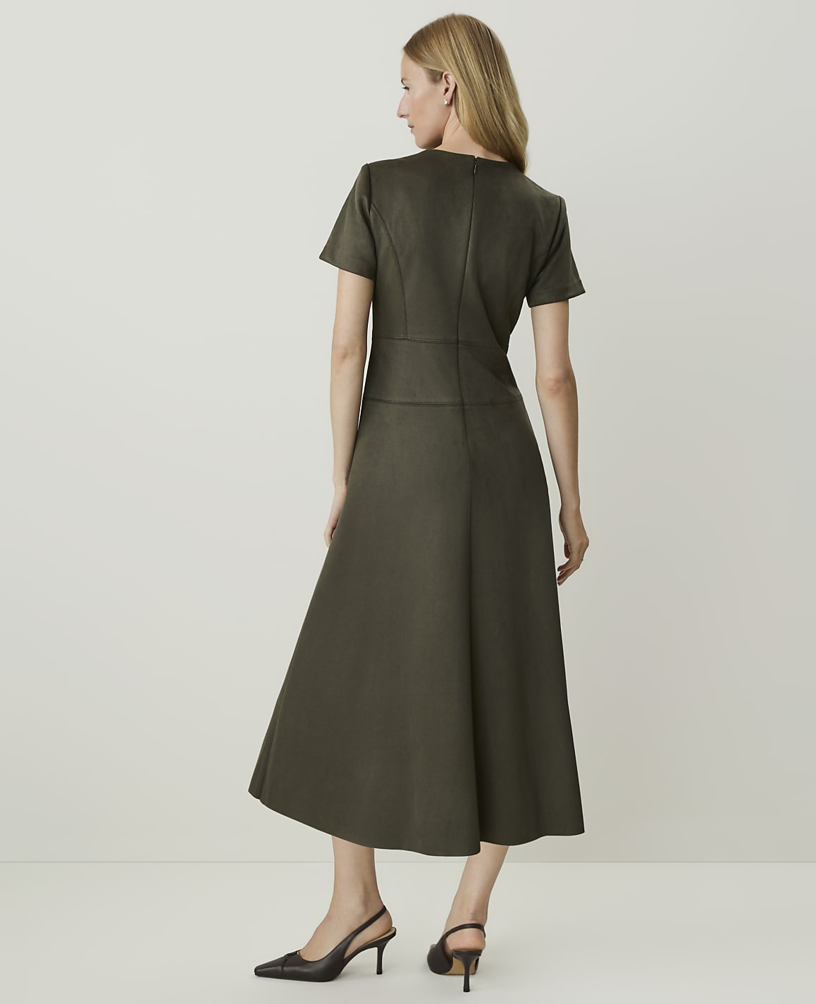 A woman in a dark green dress stands against a plain, light background.