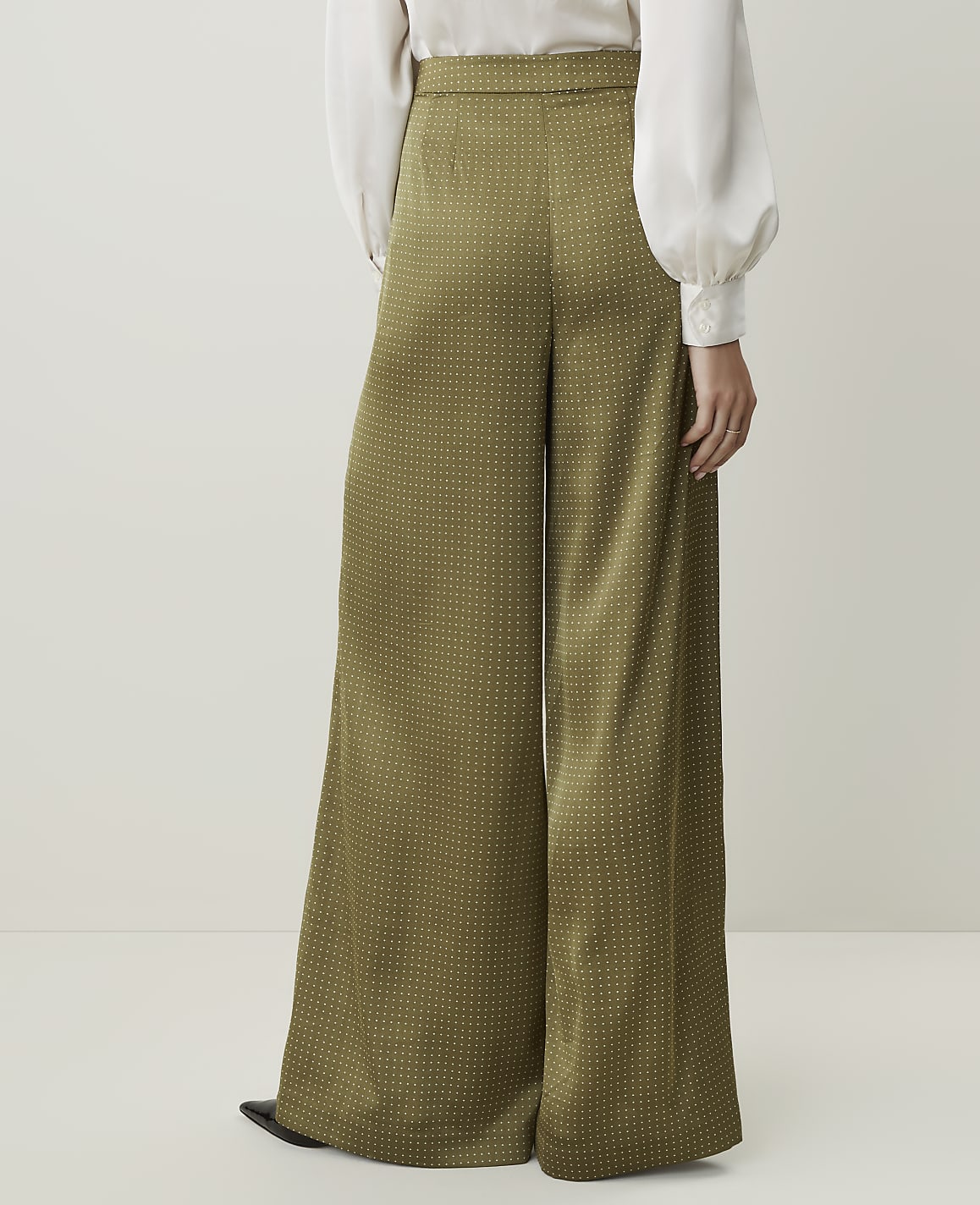 A person wearing wide-leg, olive-green patterned pants stands against a plain, light-colored background.