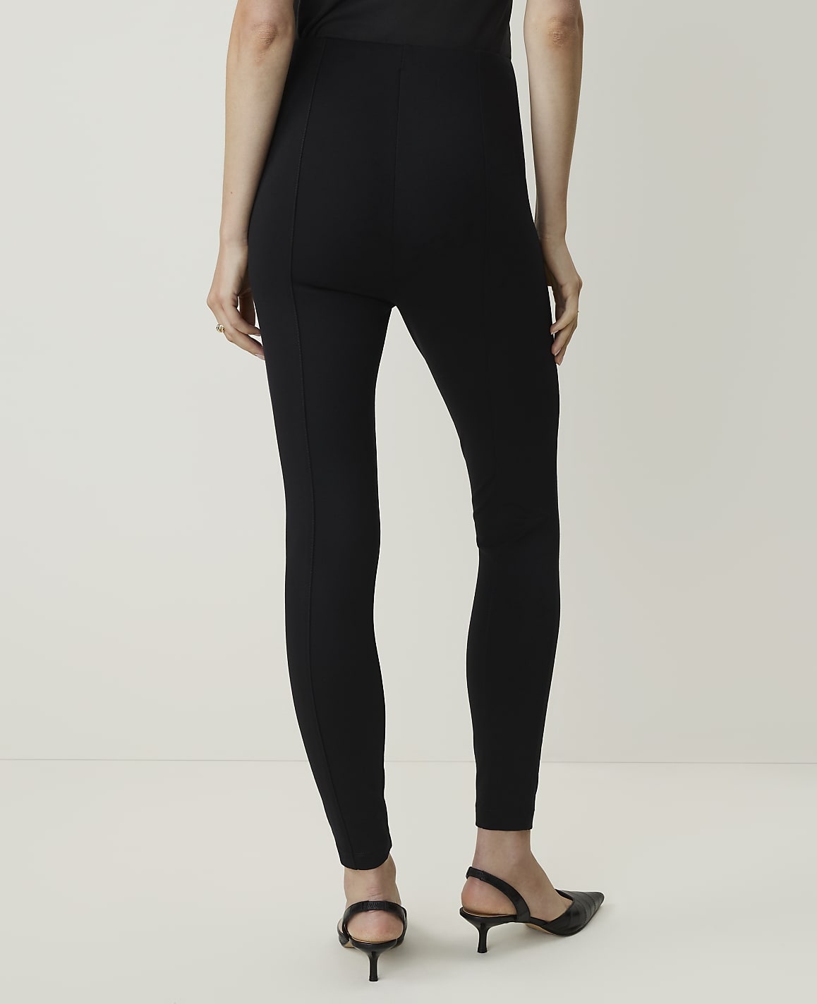 A person wearing black leggings and kitten heels stands against a plain white background.