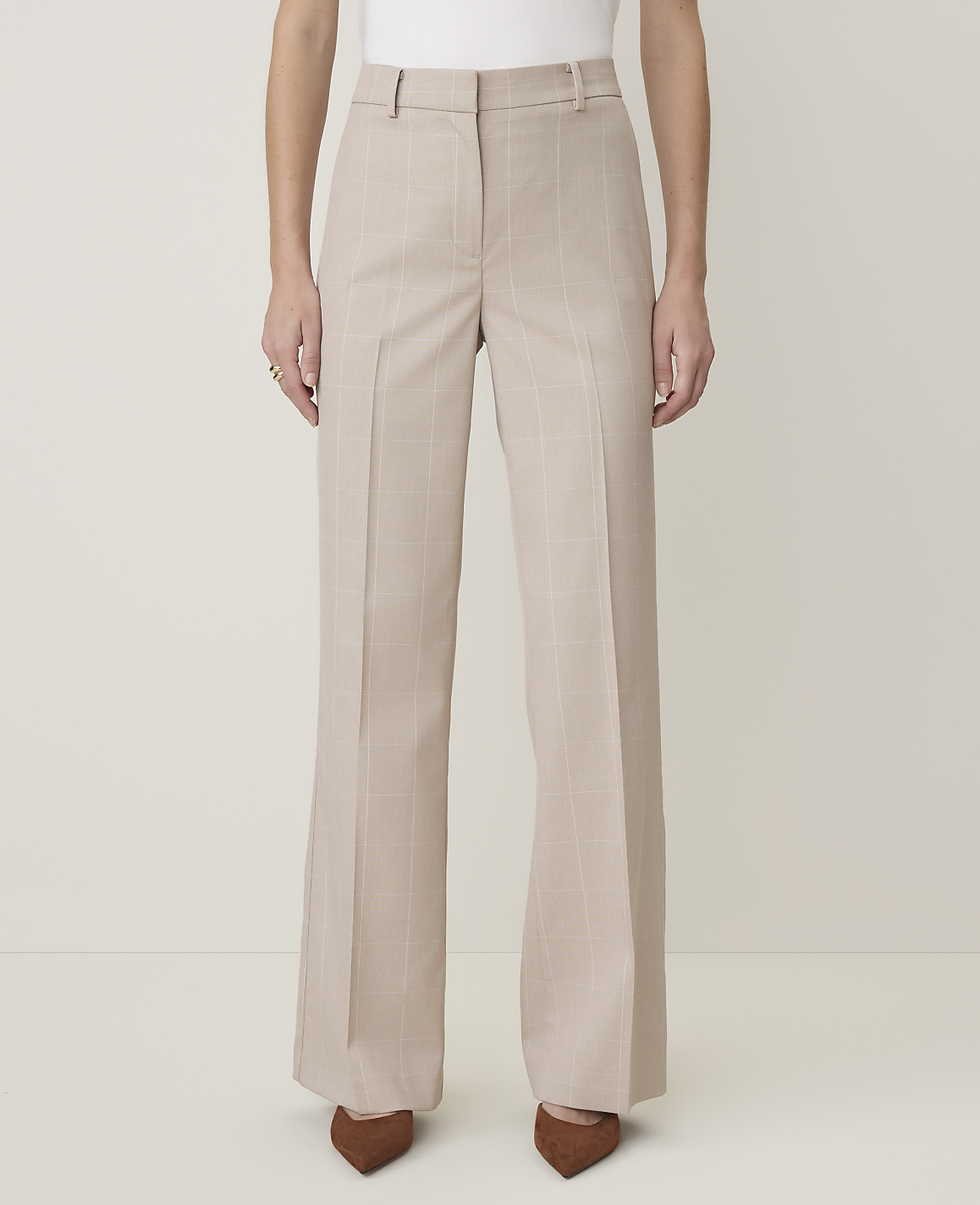 A person stands in light-colored, wide-leg trousers with subtle pinstripes, wearing brown pointed-toe heels against a plain, light background.