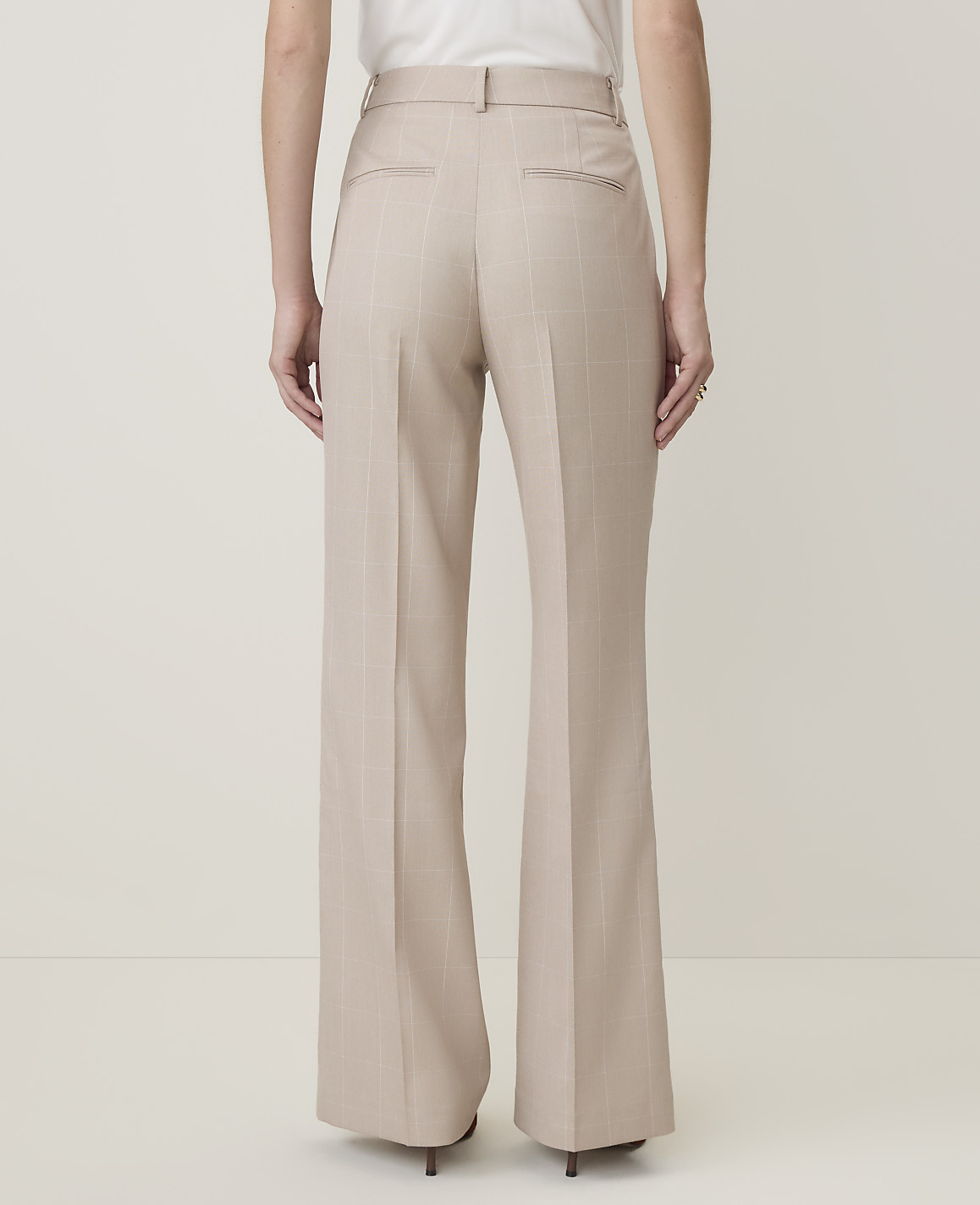 A person wearing beige wide-leg trousers stands against a plain, light-colored background.