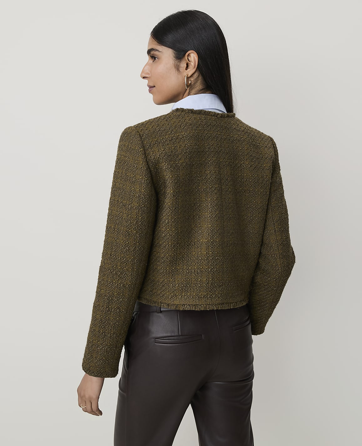 A woman in a textured green jacket and brown leather pants stands against a plain, light-colored background.