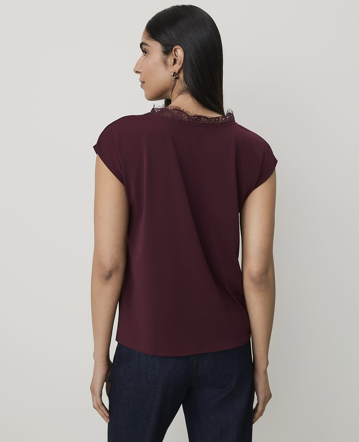 A woman in a maroon top and dark jeans stands against a plain white background.