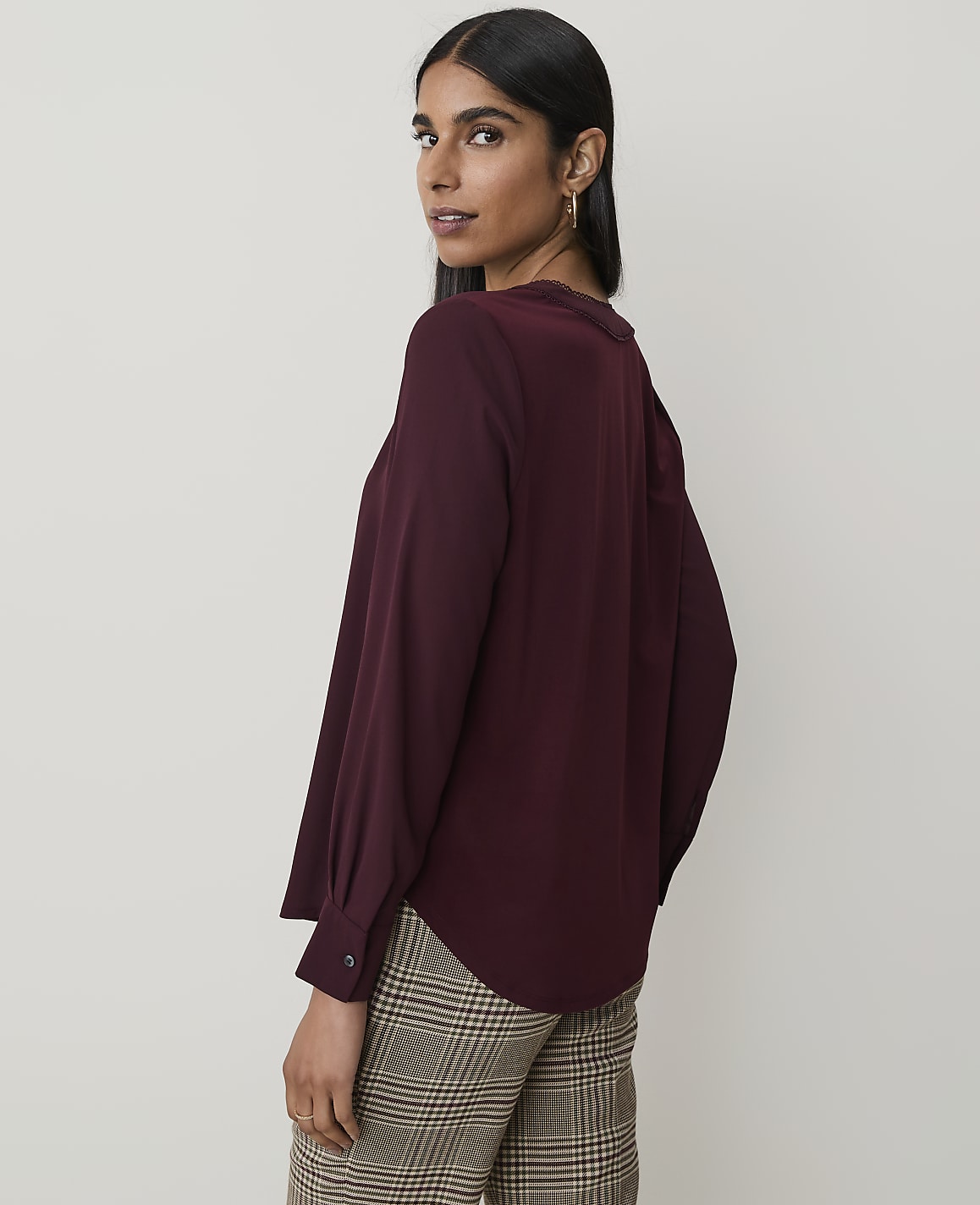 A woman in a burgundy blouse and plaid pants poses against a plain, light-colored background.