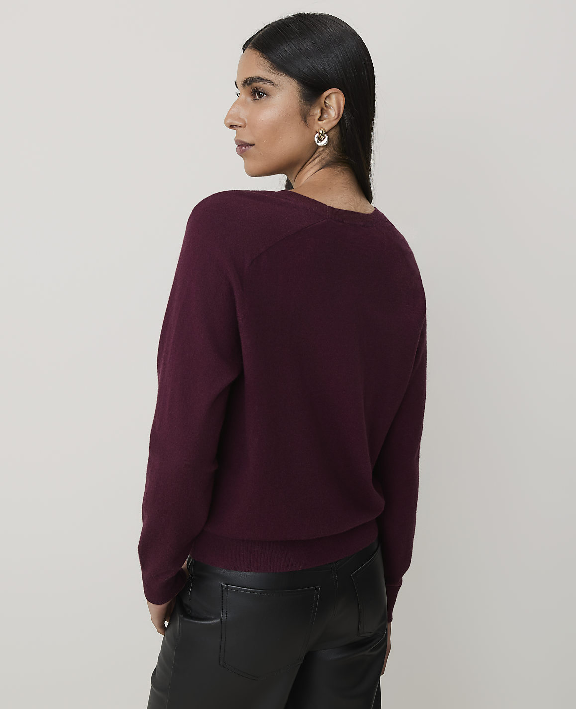 A woman in a burgundy sweater and black leather pants stands against a plain, light gray background.
