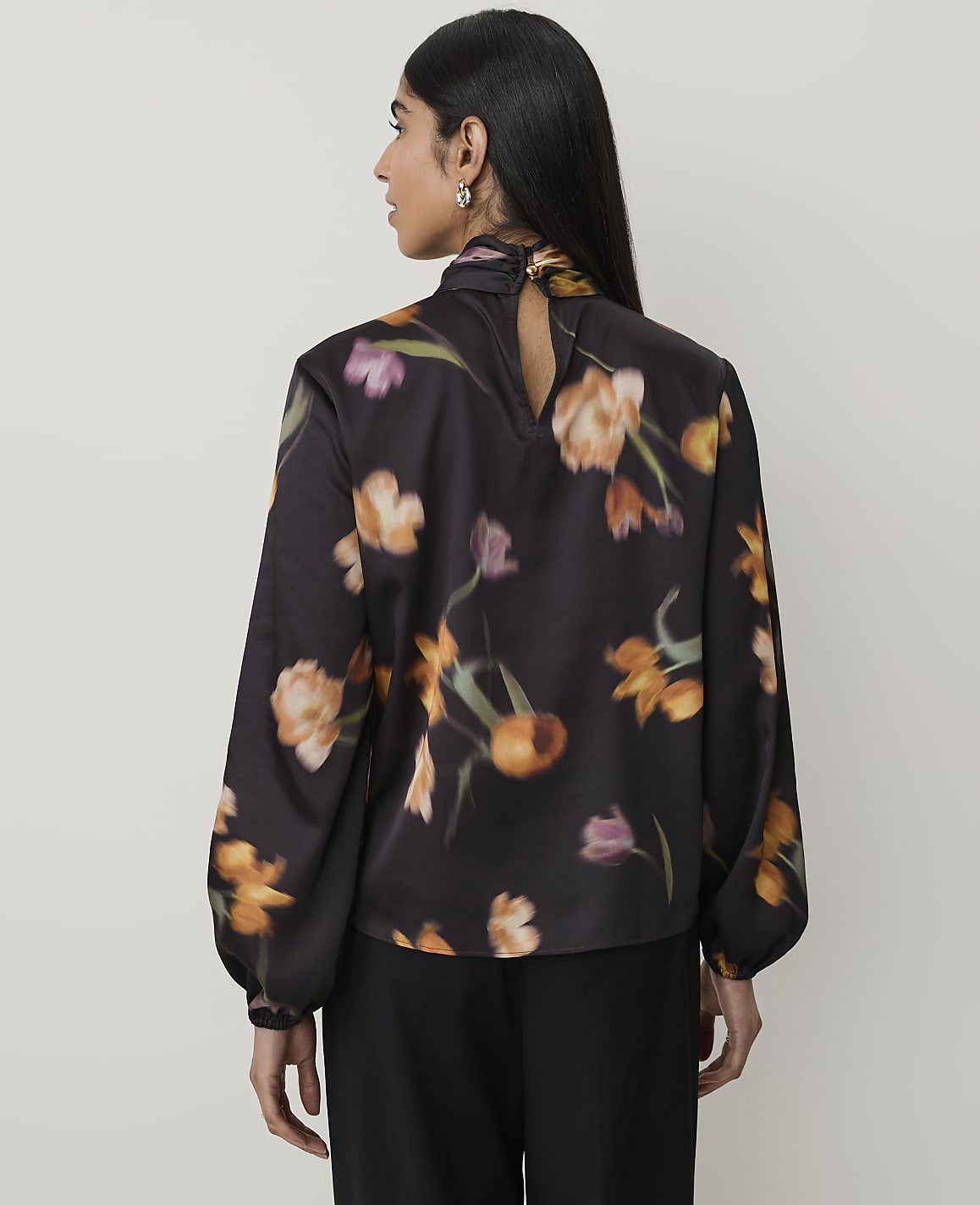 A woman in a dark floral blouse stands against a plain, light-colored background.