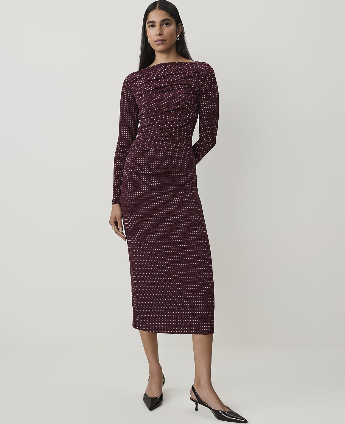 A woman in a patterned maroon dress stands against a plain white background.