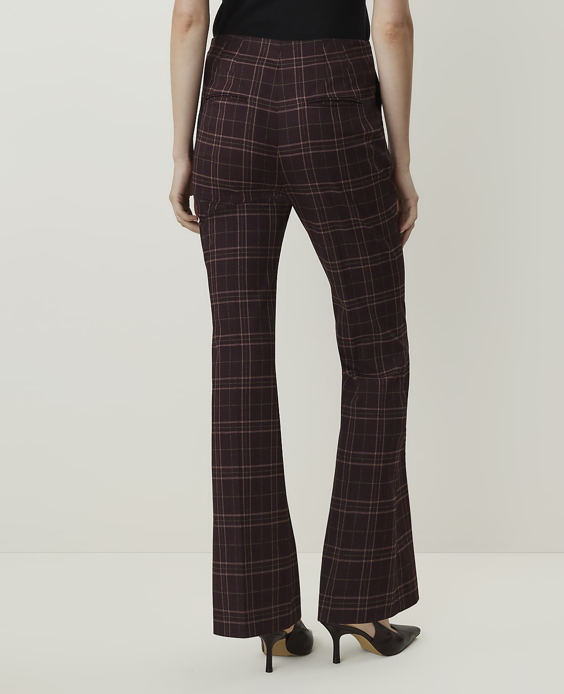 A person wearing flared plaid pants and heels stands against a plain white background.